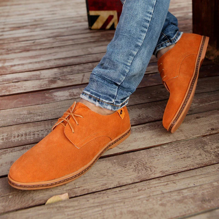 Men's orange suede casual shoes worn with rolled-up blue jeans on wooden floor