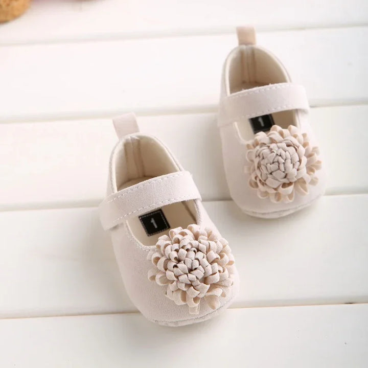 Soft beige baby shoes with strap and decorative flower detail on white wooden surface