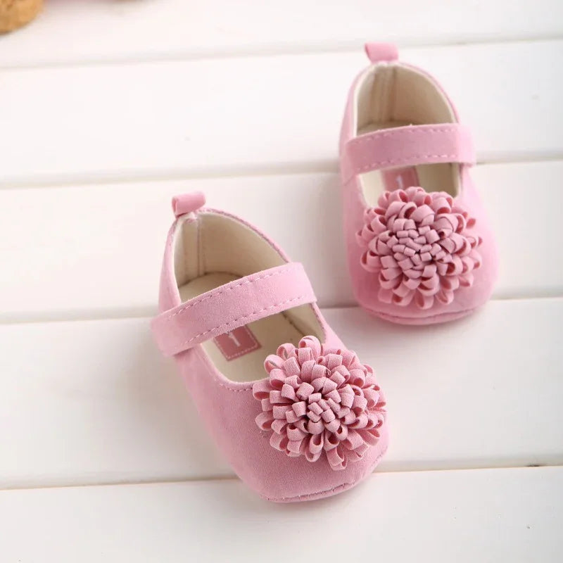 Pair of soft pink baby shoes with large fabric flower decoration on white background