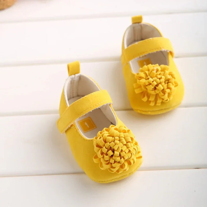 Pair of bright yellow baby shoes with textured pom-pom detail on white surface