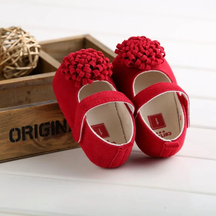 Red baby shoes with decorative bows displayed on white surface beside wooden crate