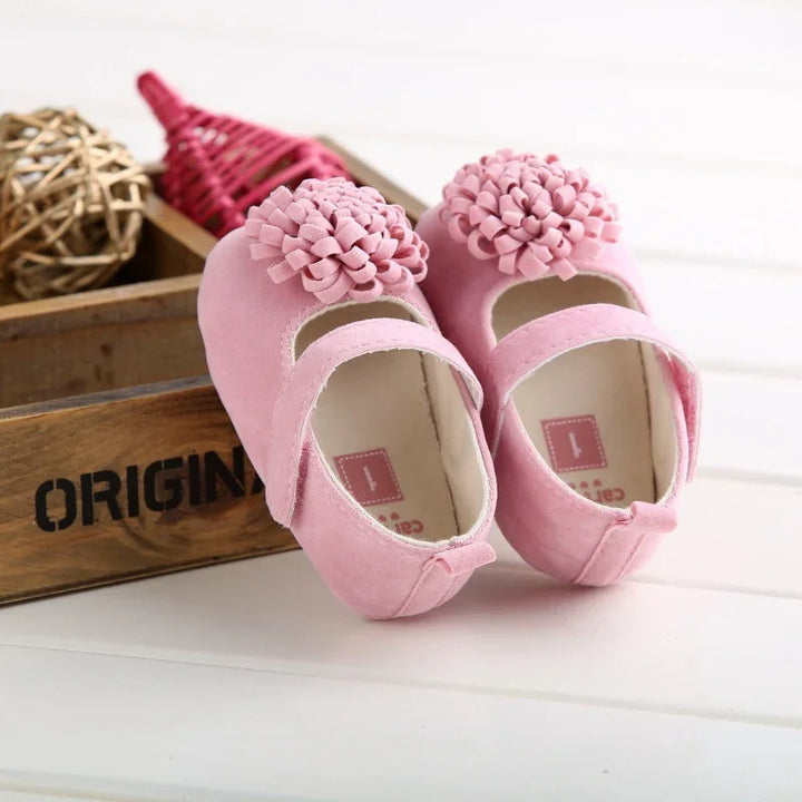Pink baby girl shoes with flower decoration on wooden crate background