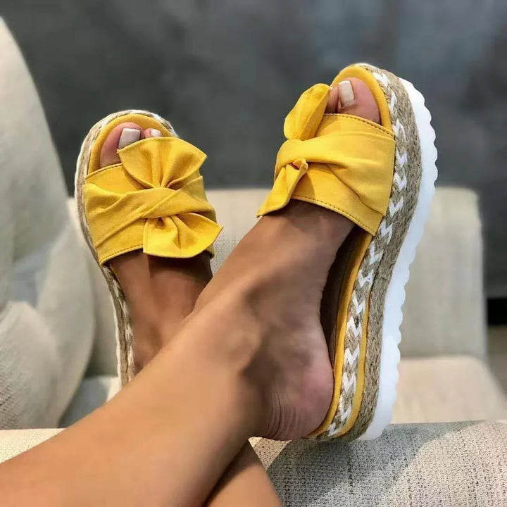 Close-up of feet wearing yellow platform sandals with bow detail and woven jute sole