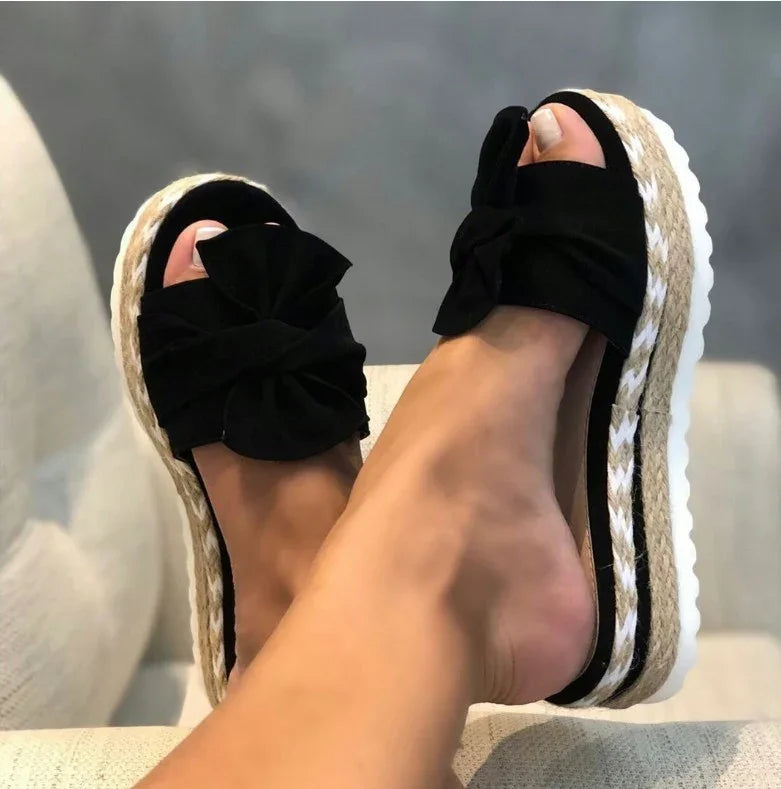 Close-up of feet wearing black bow espadrille platform sandals with woven jute soles