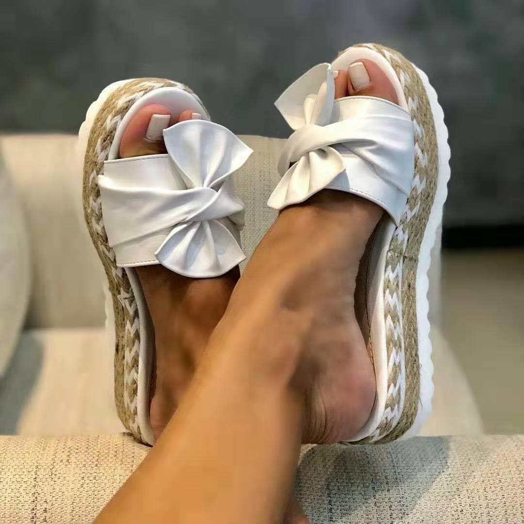 Close-up of feet wearing white bow espadrille sandals with woven platform soles on beige fabric