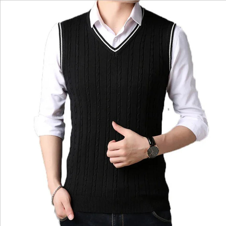 Man wearing black cable knit V-neck sweater vest over white shirt with rolled sleeves