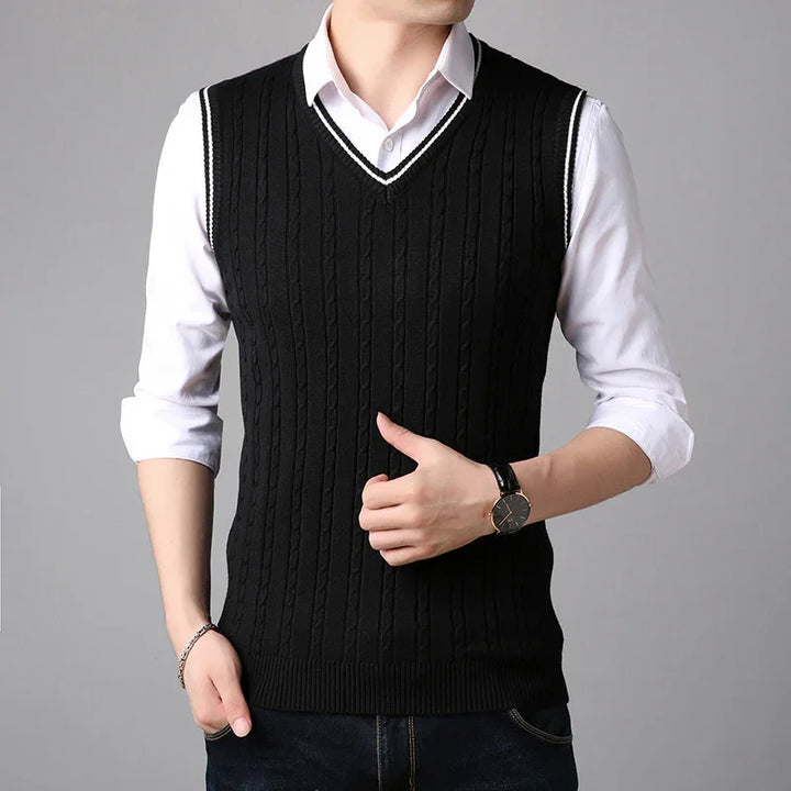Man wearing black cable knit sleeveless sweater vest over white dress shirt with rolled sleeves