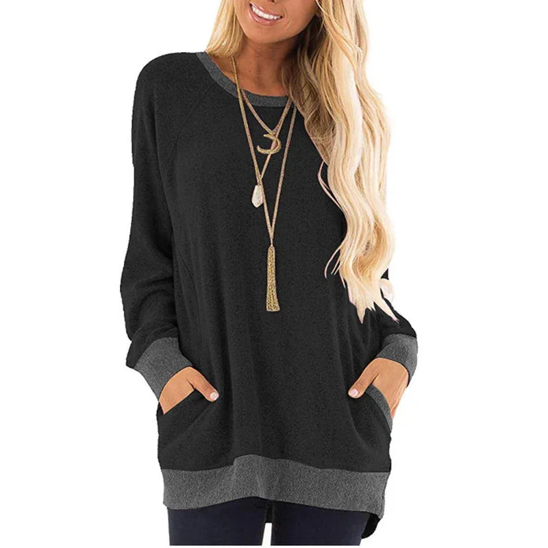 Woman wearing black long sleeve tunic with grey cuffs and hem, featuring two front pockets and layered necklaces