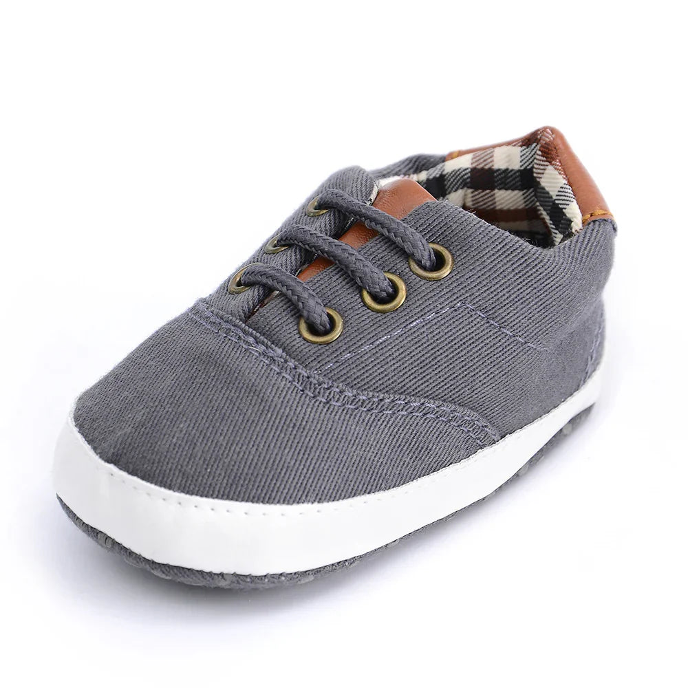 Gray baby sneaker with white sole, plaid inner lining, and brown leather accent on tongue and heel