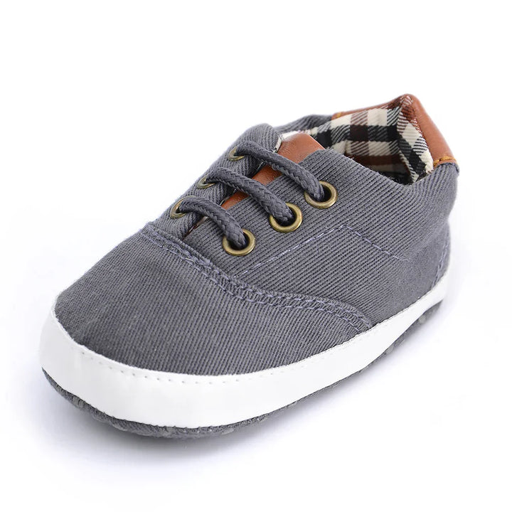 Gray baby sneaker with white sole, plaid inner lining, and brown leather accent on tongue and heel