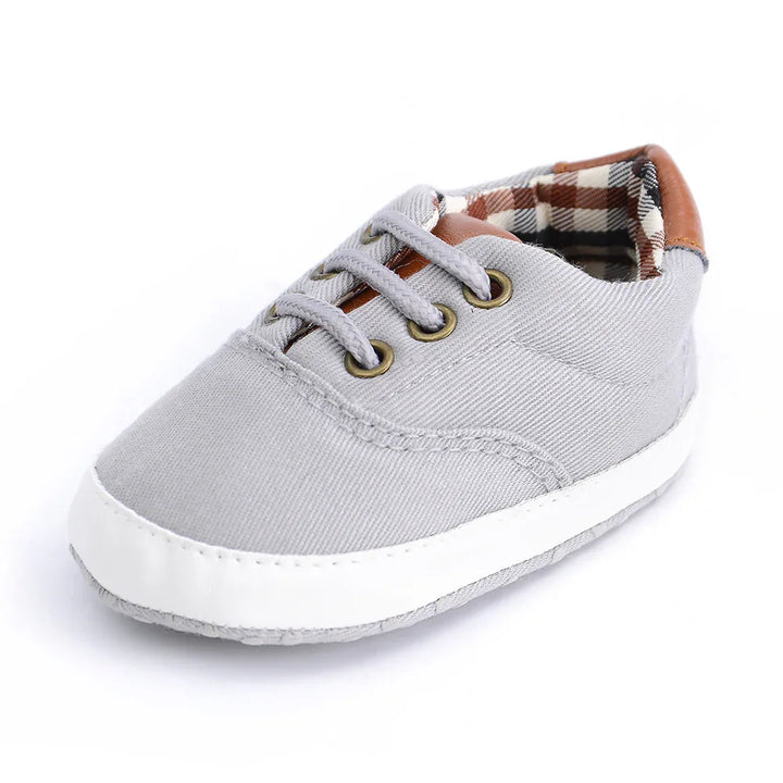 grey baby sneaker with white sole, brown plaid inner lining, and grey laces