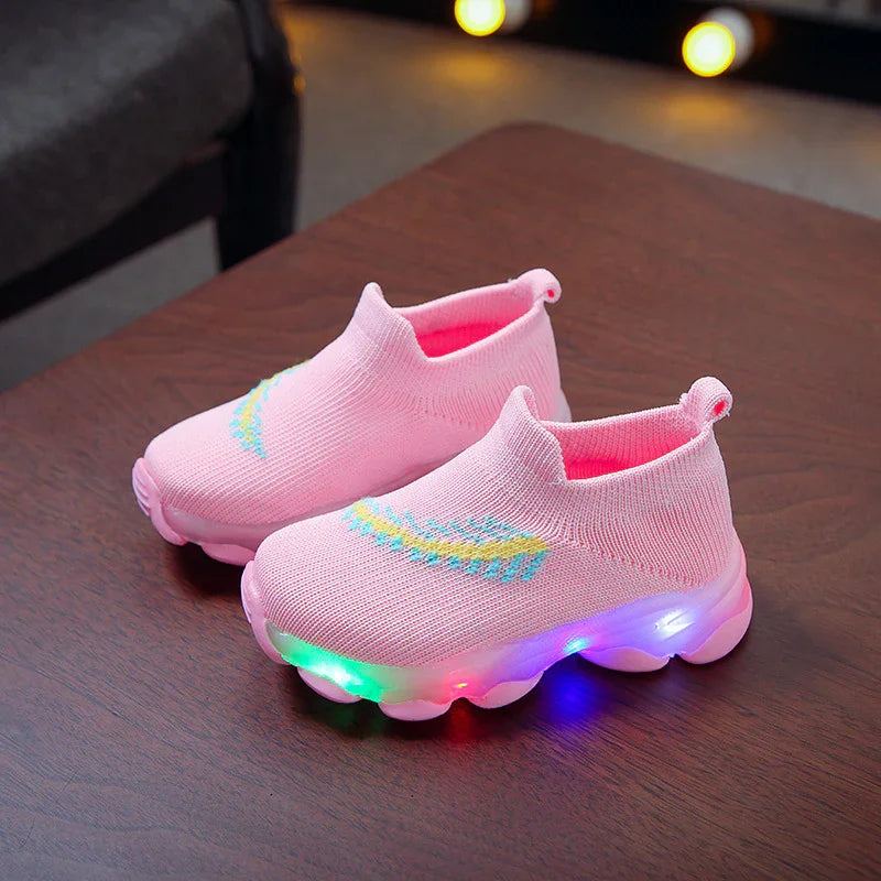 Pink toddler light-up sneakers with knitted upper and colorful sole lights on wooden table