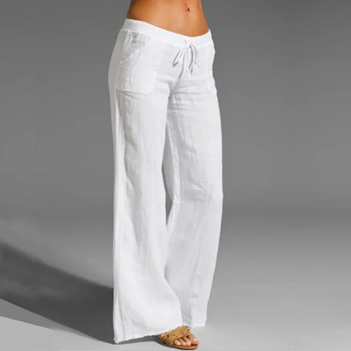 Woman wearing white wide-leg linen pants with drawstring waist and pockets, paired with sandals