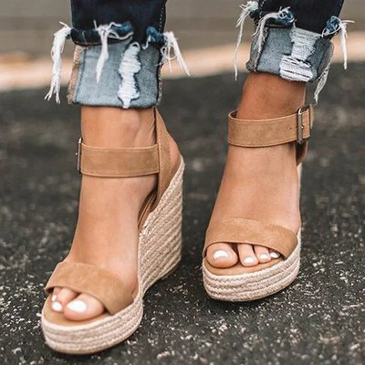 Woman wearing tan suede wedge sandals with ankle straps and distressed rolled-up jeans on pavement