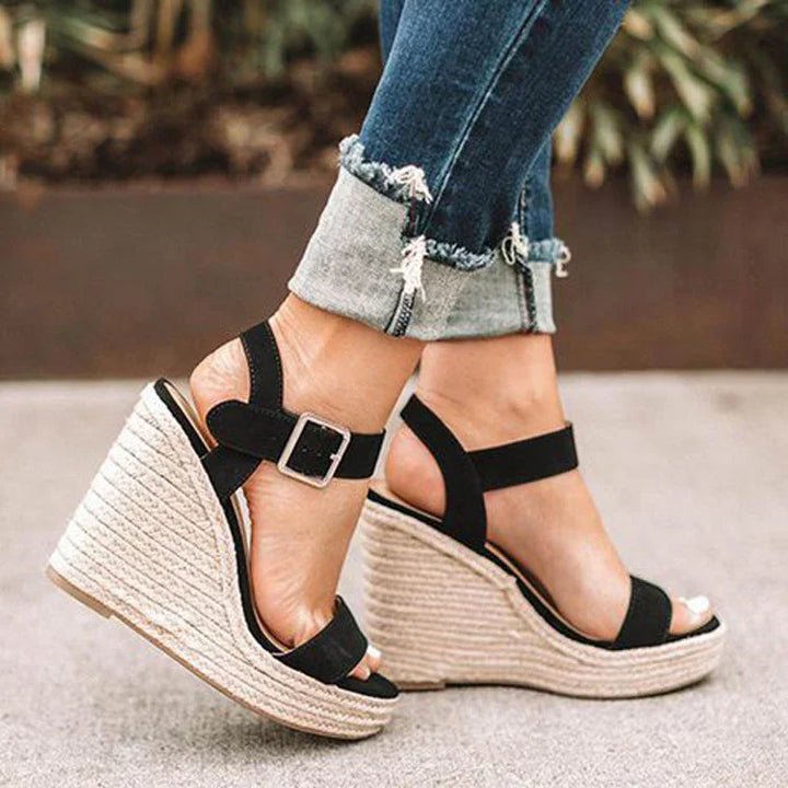 Black ankle strap wedge sandals with woven platform heels worn with cuffed skinny jeans