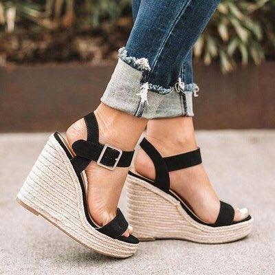 Black suede wedge sandals with ankle straps paired with rolled-up distressed skinny jeans on concrete floor