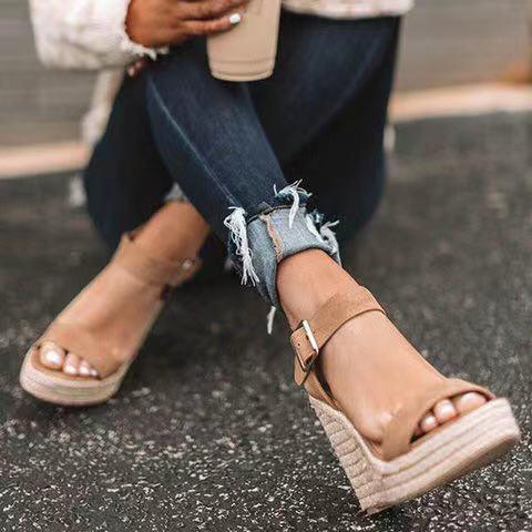 close-up of woman's feet with beige wedge sandals and frayed hem dark blue jeans on asphalt