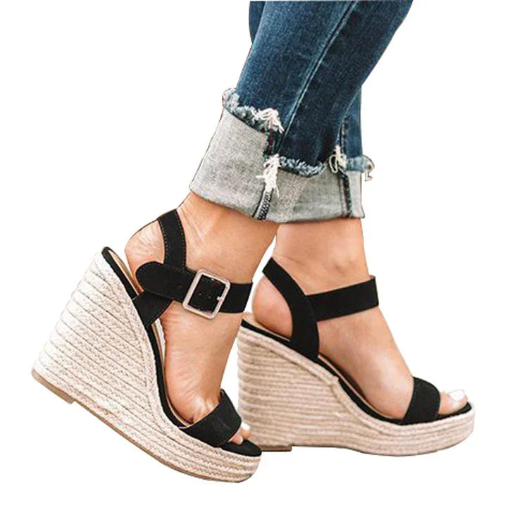 Black strappy wedge sandals with buckle over rolled-up blue jeans on feet