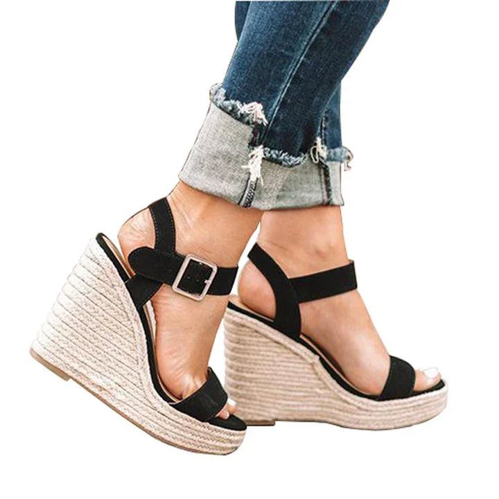 Black strappy wedge sandals with buckle over rolled-up blue jeans on feet