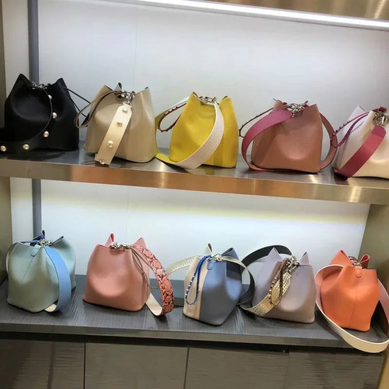 Colorful leather bucket handbags with wide straps displayed on shelves in a retail store