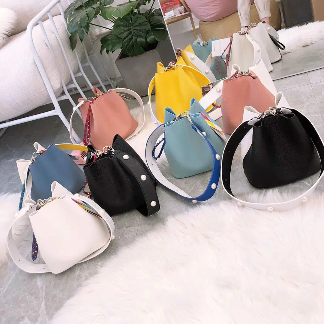 Colorful leather bucket bags with pearl-embellished straps displayed on a gray floor and white furry rug