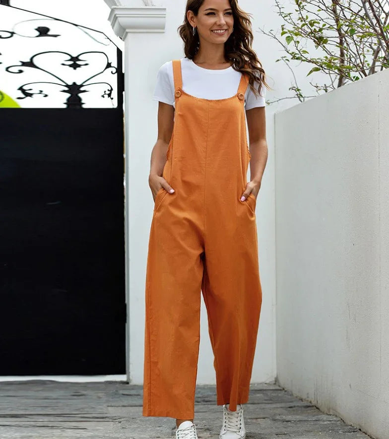 Smiling woman wearing orange wide-leg jumpsuit with white t-shirt and sneakers standing outdoors