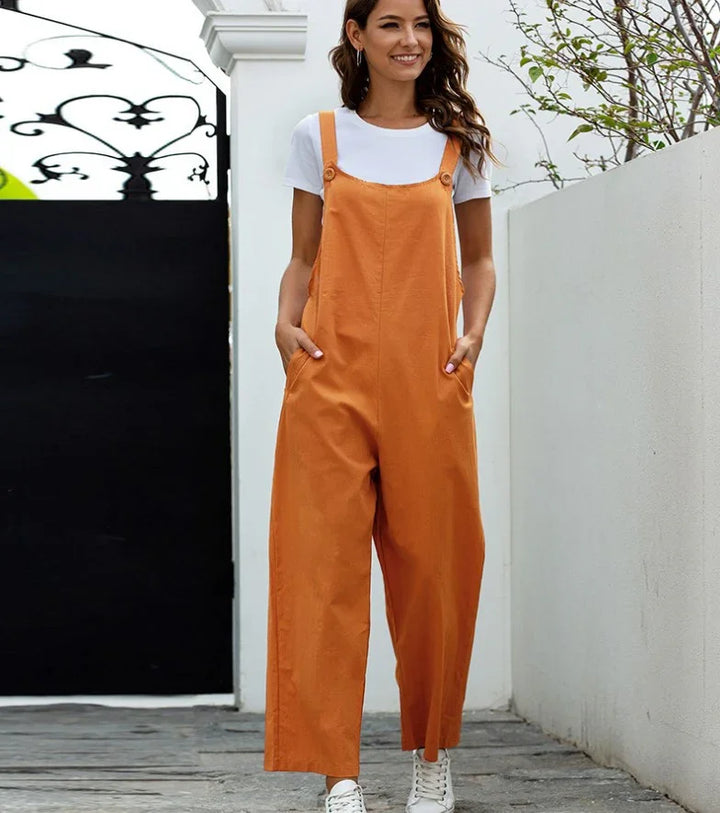 Smiling woman wearing orange wide-leg jumpsuit with white t-shirt and sneakers standing outdoors