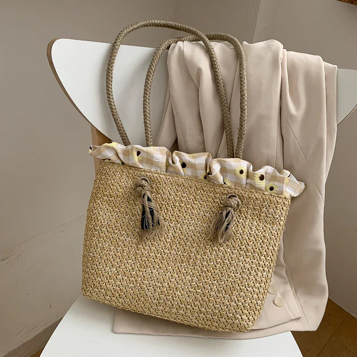Woven straw handbag with floral fabric lining and tassels on white chair draped with beige coat