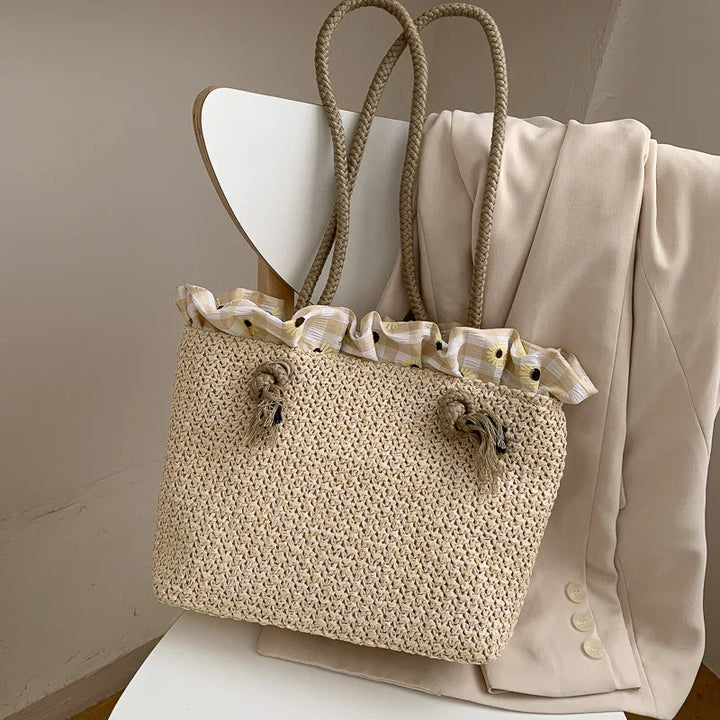 Beige woven summer tote bag with floral ruffled fabric lining, hanging on chair with cream blazer