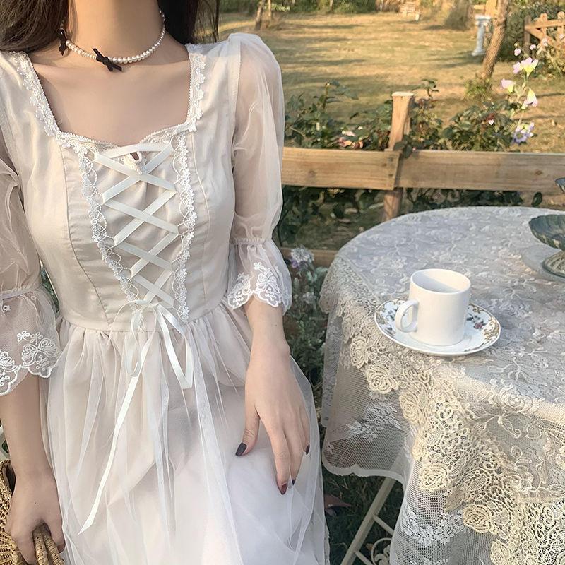 Woman in white lace-up vintage dress sitting outdoors near table with lace tablecloth and teacup