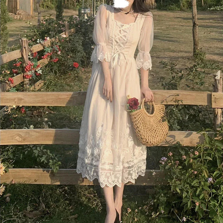 Woman in vintage lace white dress holding woven straw bag with roses by wooden fence in garden