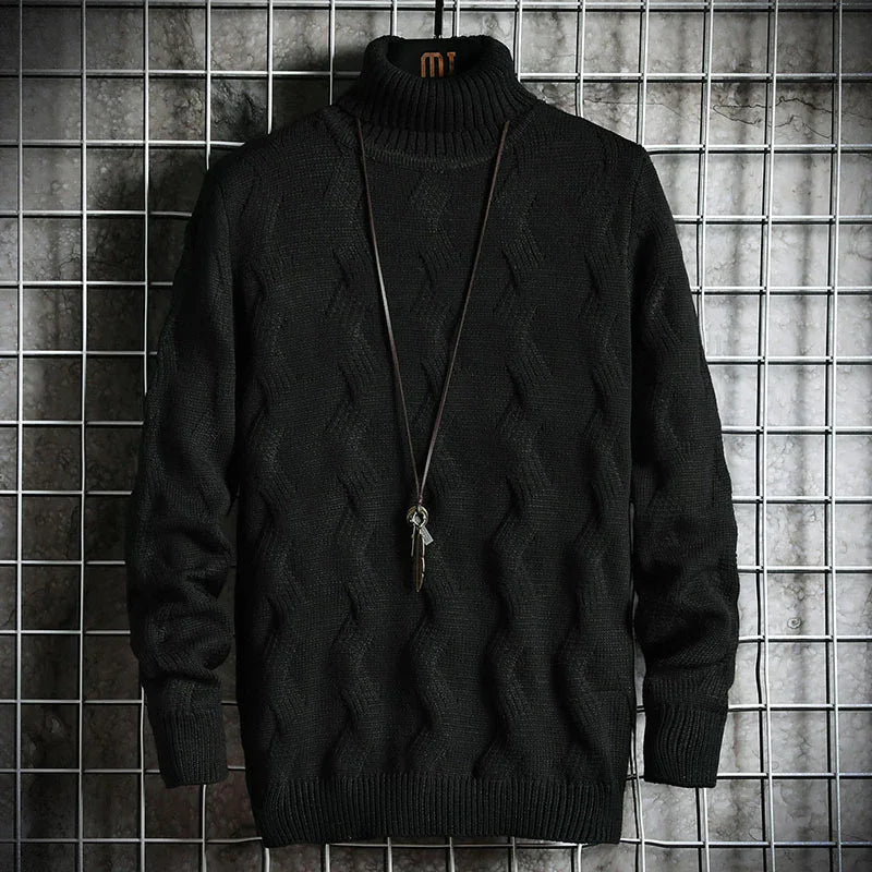 Black cable knit turtleneck sweater with long sleeves displayed on metal grid backdrop with pendant necklace