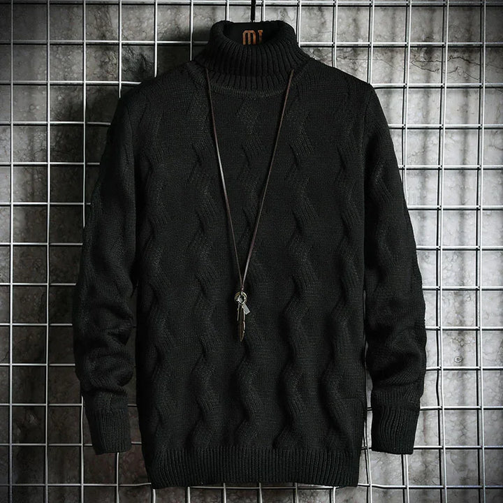 Black cable knit turtleneck sweater with long sleeves displayed on metal grid backdrop with pendant necklace