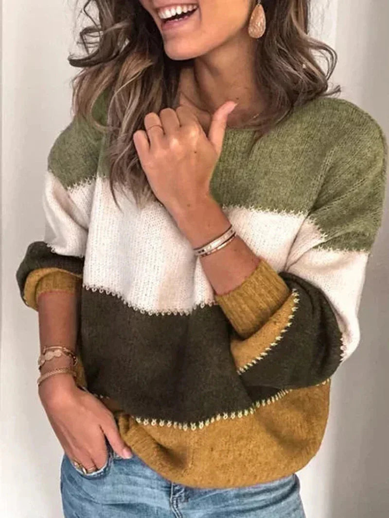 Woman wearing color-blocked knit sweater with green, white, olive, and mustard stripes, paired with blue jeans