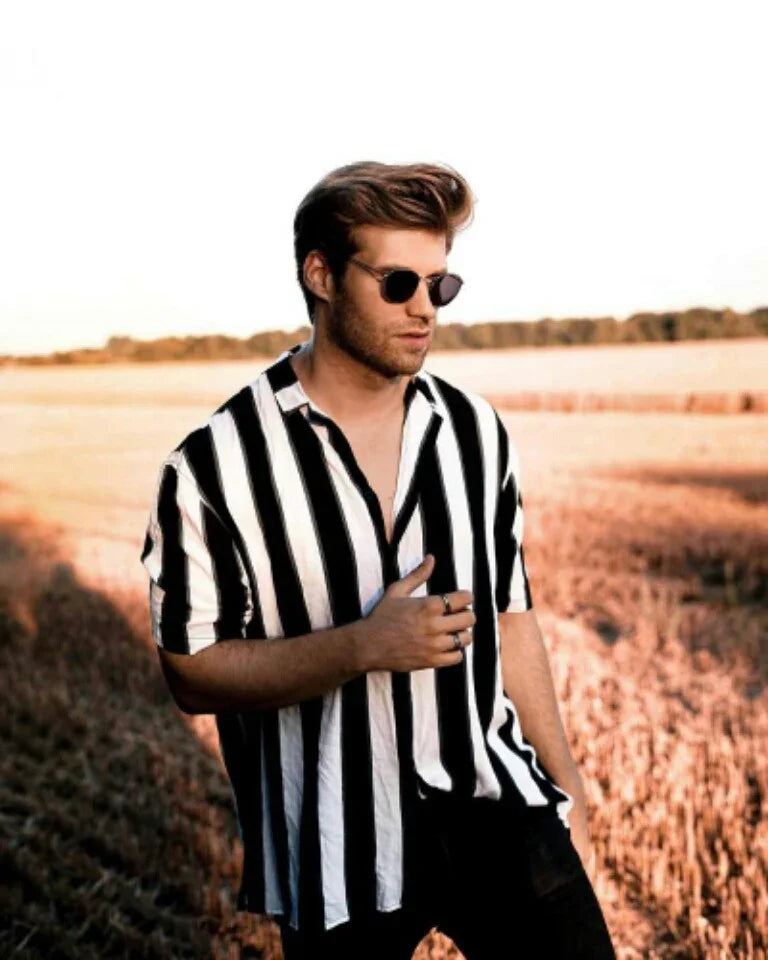 Young man wearing black and white striped shirt and sunglasses standing in a golden field at sunset