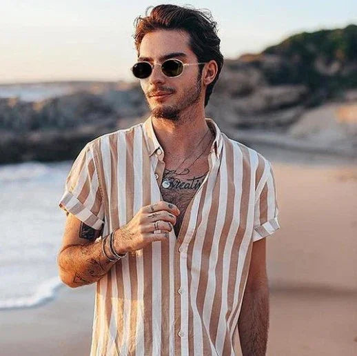 Young man wearing striped short-sleeve shirt and sunglasses on beach at sunset