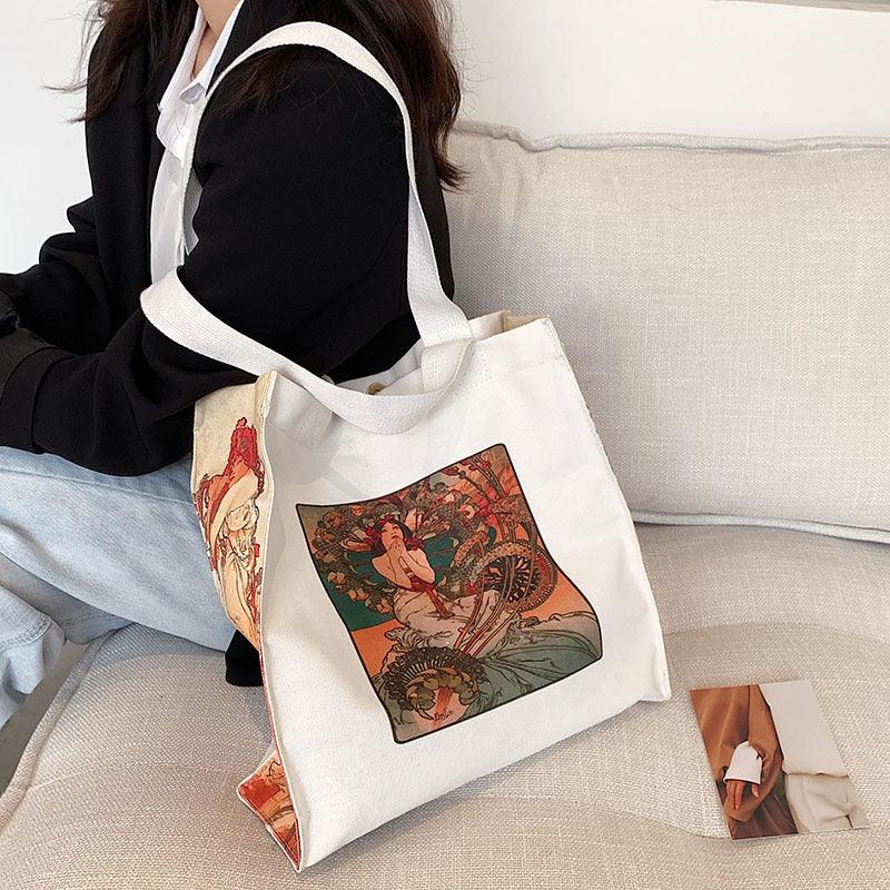 White canvas tote bag with vintage art print featuring a woman and dragon, worn by person in black jacket