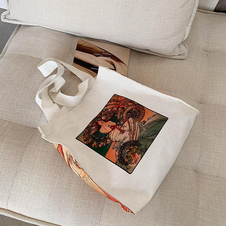 White canvas tote bag with vintage art print featuring a woman holding a fan, placed on beige fabric sofa