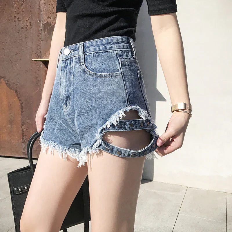 Woman wearing distressed blue denim shorts with cut-out and studded strap detail on thigh