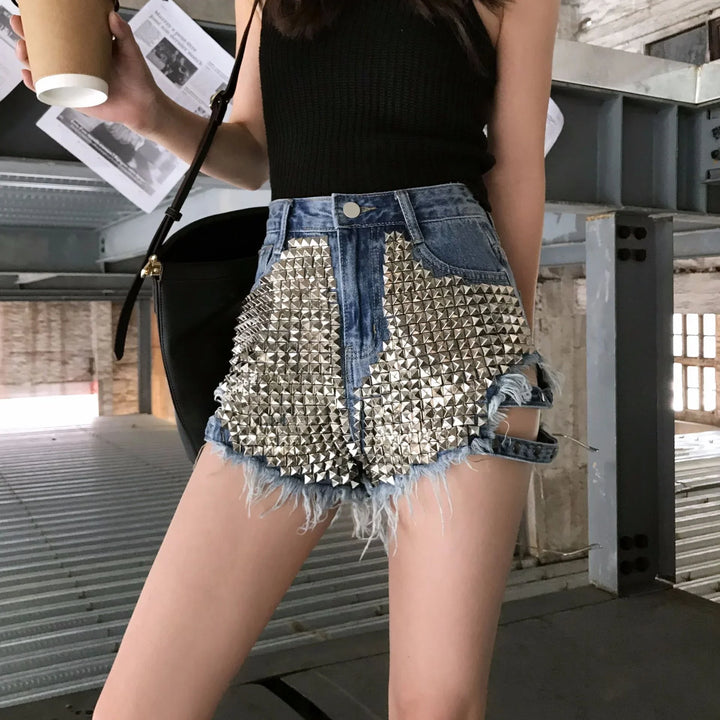 Woman wearing black top and distressed denim shorts with silver stud embellishments holding coffee cup