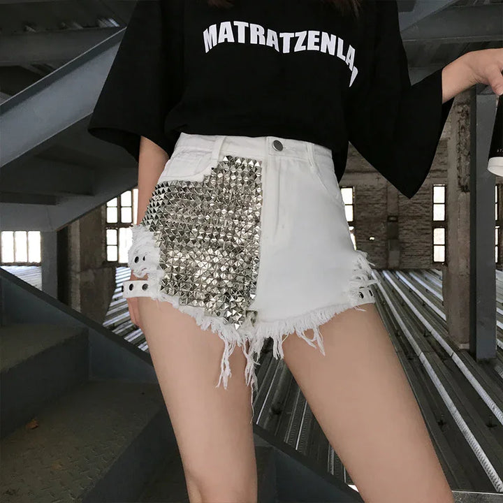 Woman wearing white distressed denim shorts with silver studs and black graphic t-shirt in industrial setting