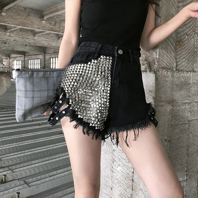 Woman wearing black denim shorts with silver pyramid studs and frayed edges holding plaid clutch