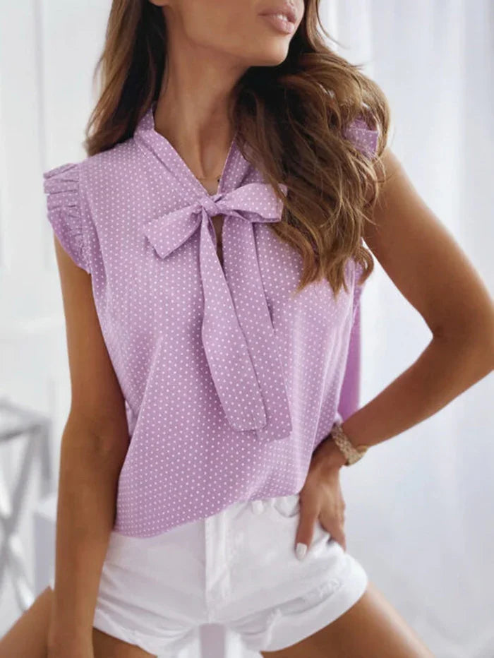 Woman wearing lavender polka dot sleeveless blouse with bow tie and white shorts indoors
