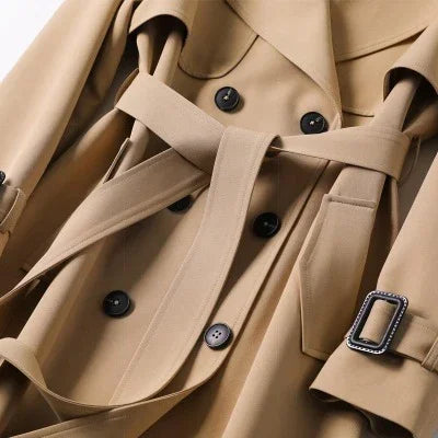 Close-up of beige trench coat with black buttons, belt, and stitched buckle detail on sleeve