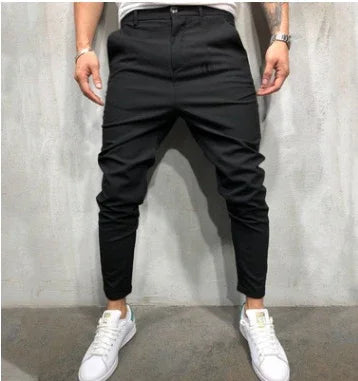 Man wearing slim fit black jogger pants with white sneakers against gray wall