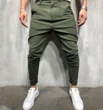 Man wearing slim fit olive green jogger pants with white sneakers against gray background