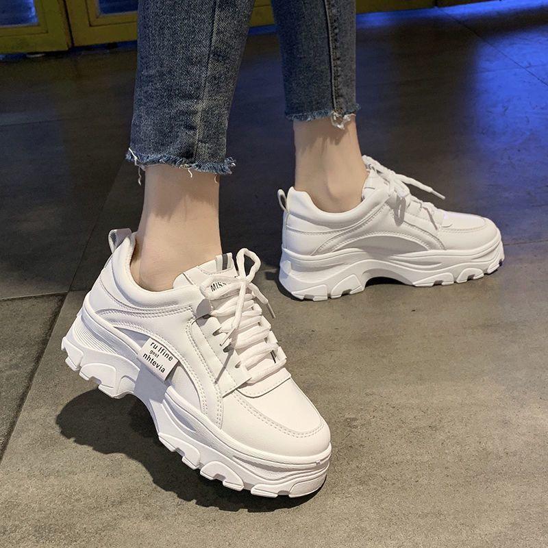 Chunky white platform sneakers with thick textured soles worn with frayed hem denim jeans on indoor concrete floor
