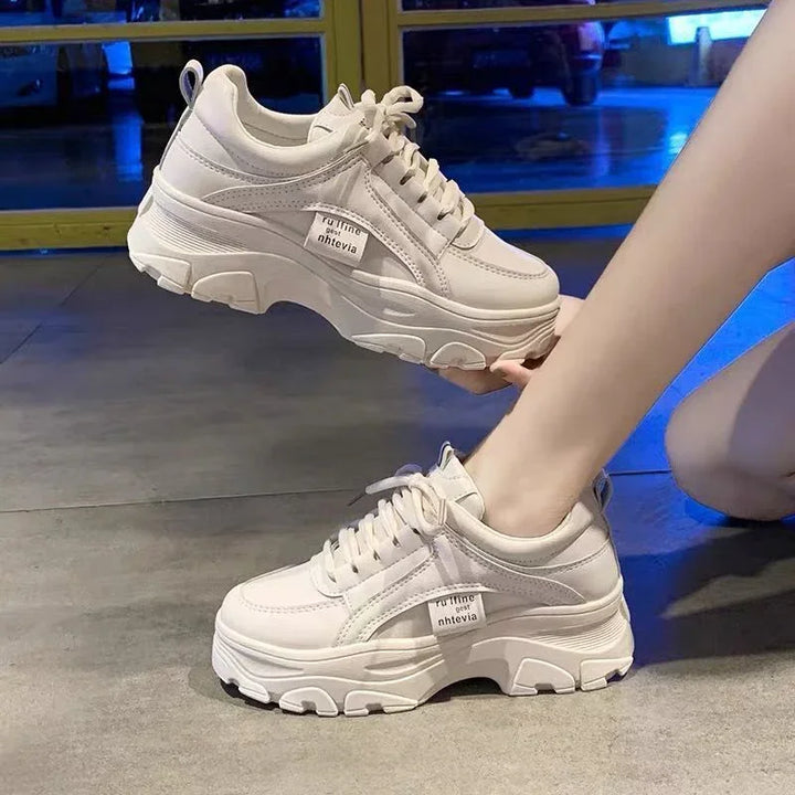 Chunky white platform sneakers with lace-up design worn by person indoors on tiled floor