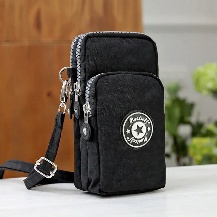 Compact black crossbody bag with dual zippered compartments and adjustable strap on white surface