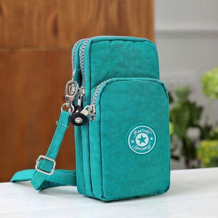 Teal crossbody sling bag with multiple zippered compartments and adjustable strap on white surface